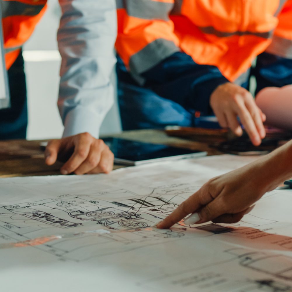 Closeup of team of industrial engineers meeting analyze machinery blueprints consult project on table in manufacturing factory. Working in manufacturing plant or production plant concept.